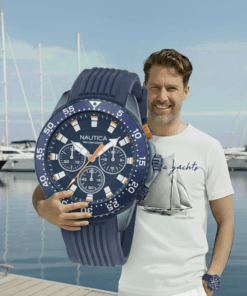 Mężczyzna w koszulce żeglarskiej Classic Yachts Columbia Black prezentuje zegarek Nautica One Sporty na tle jachtów w marinie