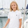 Dziewczynka w białej dziecięcej koszulce żeglarskiej polo Navinations Yacht Club